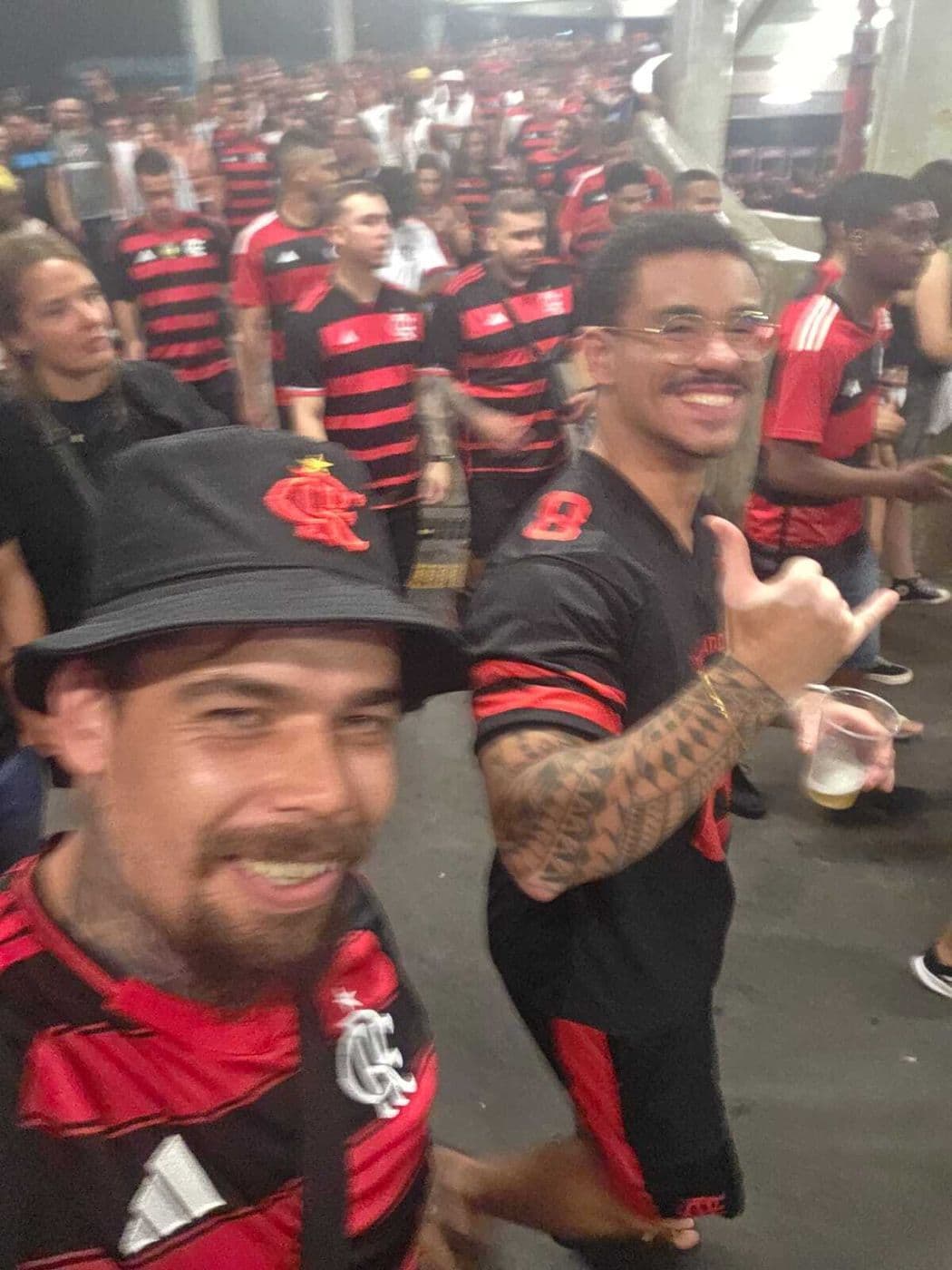 A host in a bucket hat with a guest on the stadium concourse at night